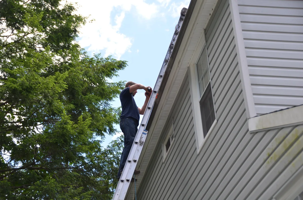Technician installing drip cap flashing to seal a flying squirrel entry point