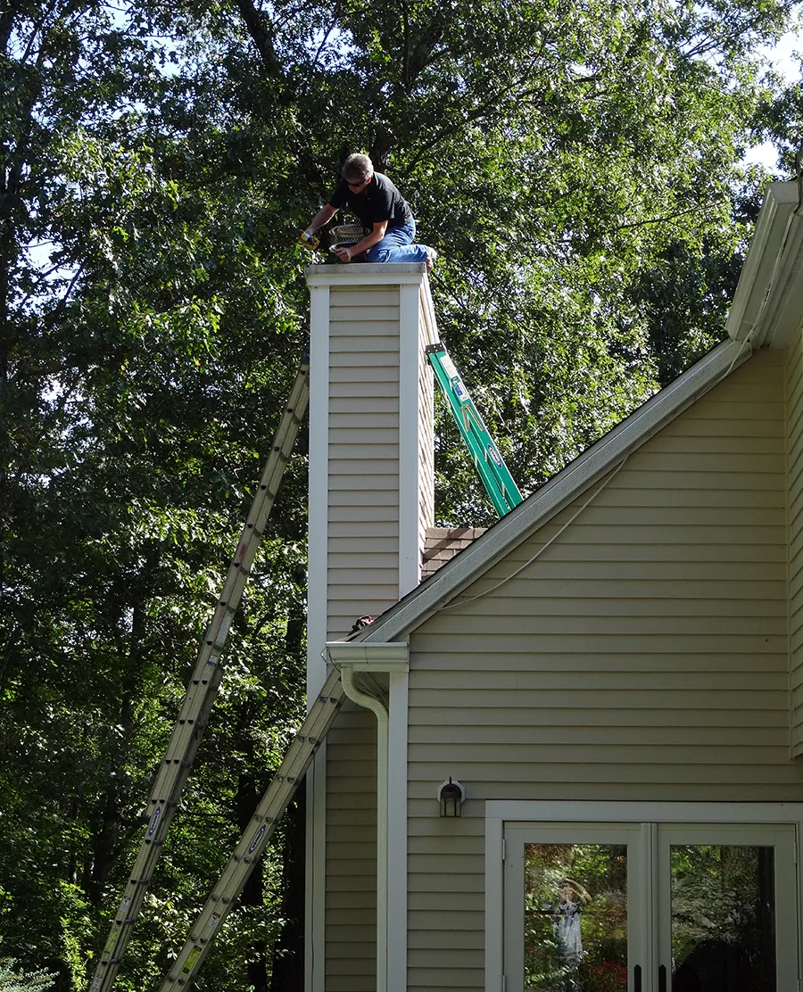 Technician on top of a chimney making repairs to seal out flying squirrels