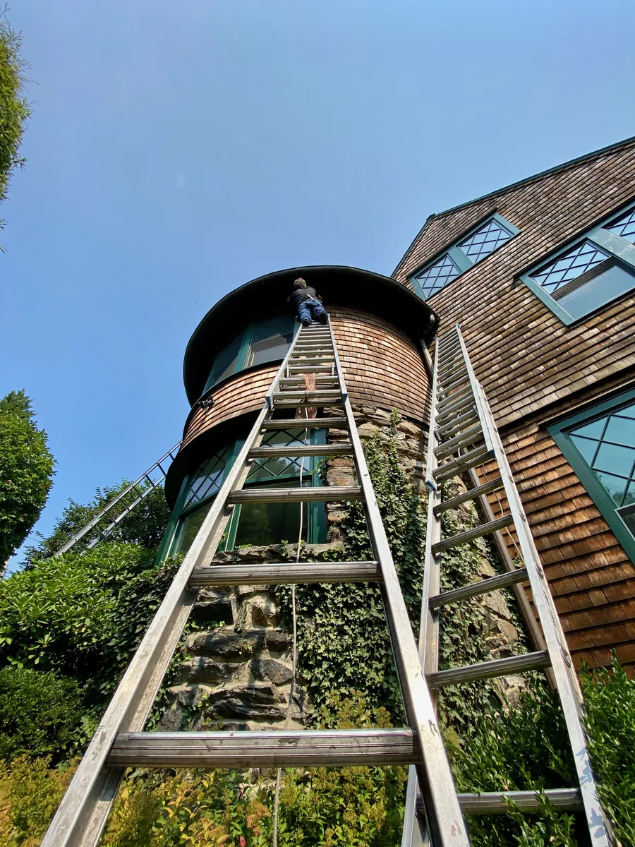 Technician on a tall ladder sealing openings in a roof turret used by flying squirrels