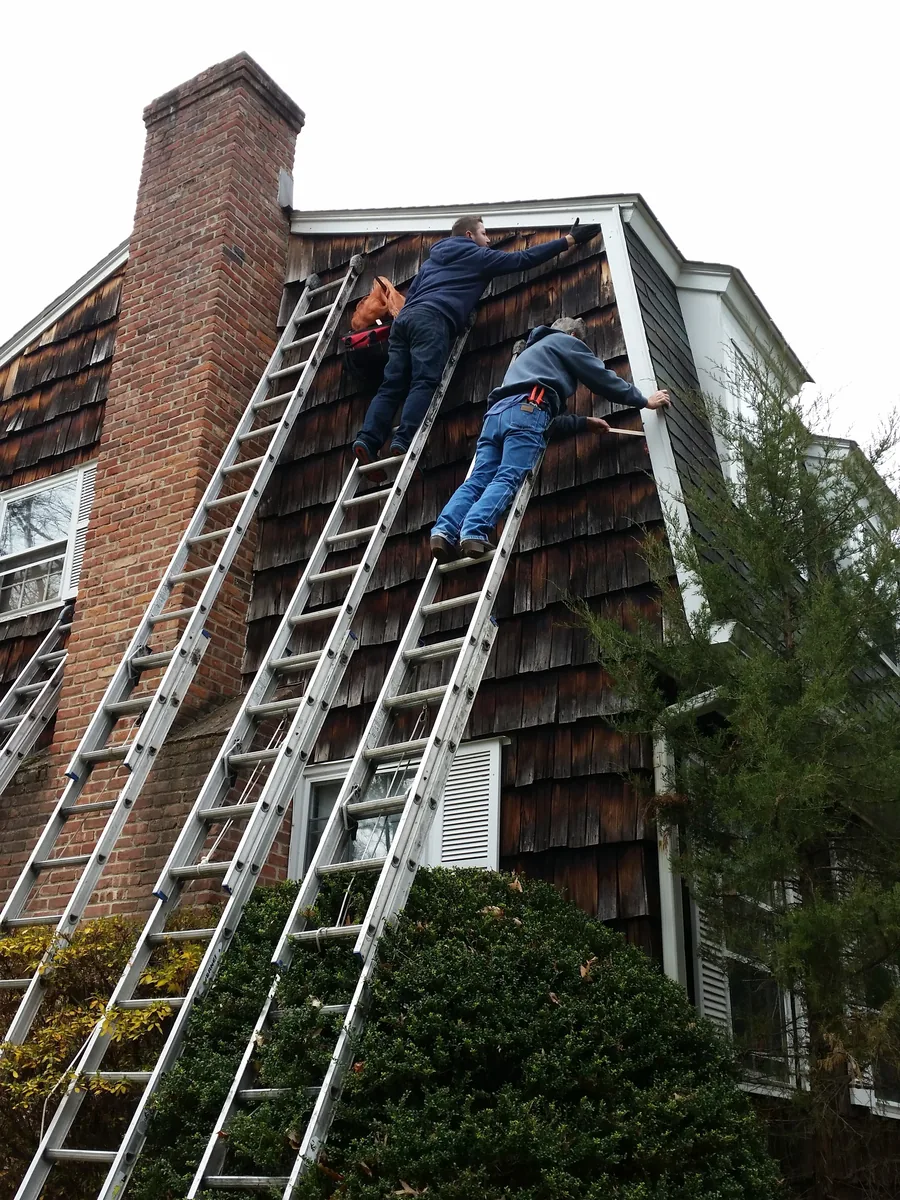 Two technicians on ladders installing copper mesh along the trim of a house