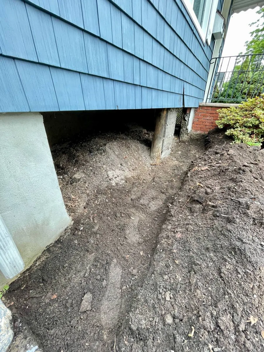 Trench dug along the base of a home leading into open crawl space area