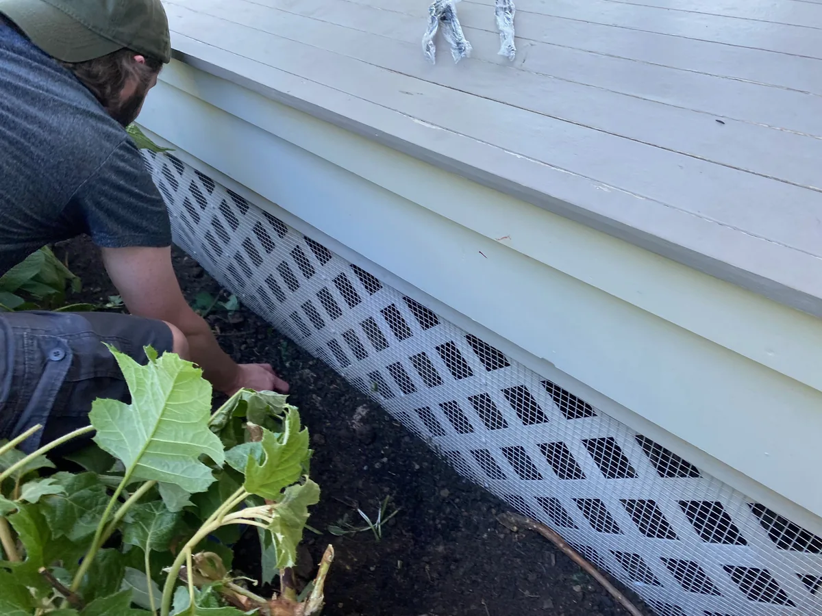 Technician installing a wildlife exclusion barrier along a deck
